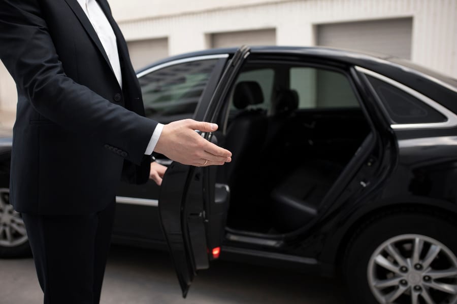 A hand opening the rear door of a black car