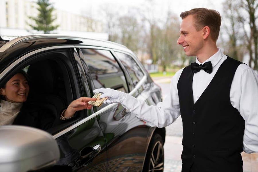 A chauffeur handing something to a passenger through the window